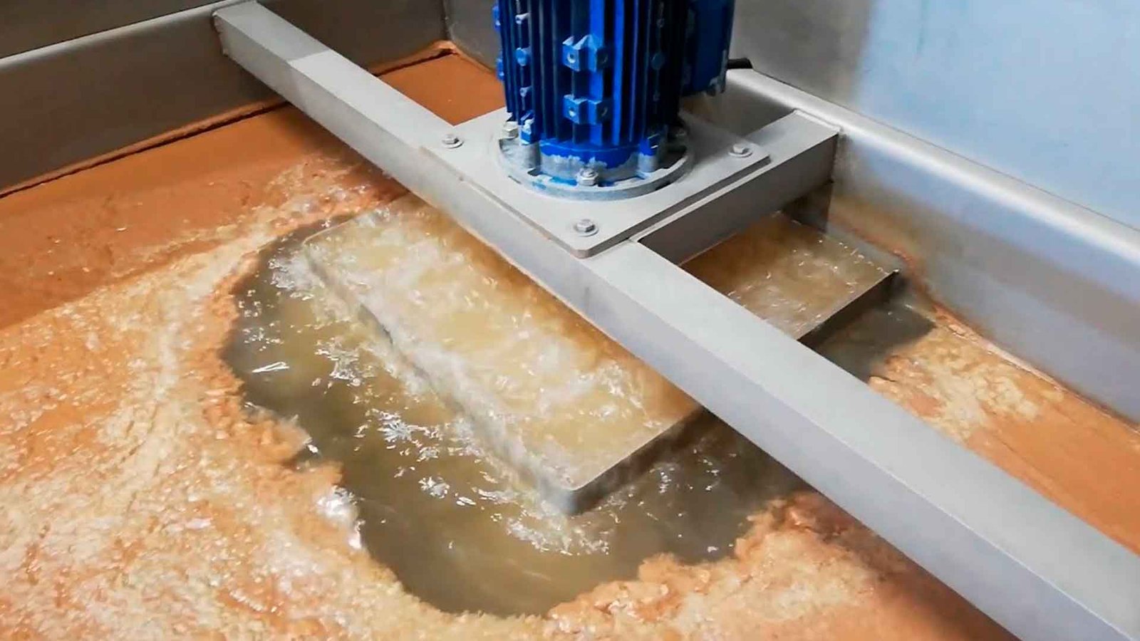 Técnico inspeccionando una planta de tratamiento de aguas residuales modular de color verde marca BIOMAX SYNERTECH, que incluye módulos de pretratamiento, decantación, DAF y oxidación avanzada. La planta está ubicada en un entorno industrial con techo alto y tuberías visibles. - ver más información