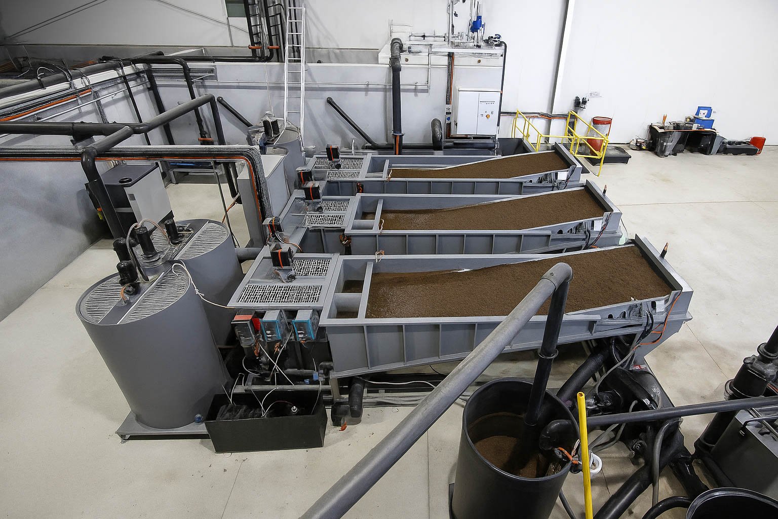 Técnico inspeccionando una planta de tratamiento de aguas residuales modular de color verde marca BIOMAX SYNERTECH, que incluye módulos de pretratamiento, decantación, DAF y oxidación avanzada. La planta está ubicada en un entorno industrial con techo alto y tuberías visibles. - ver más información