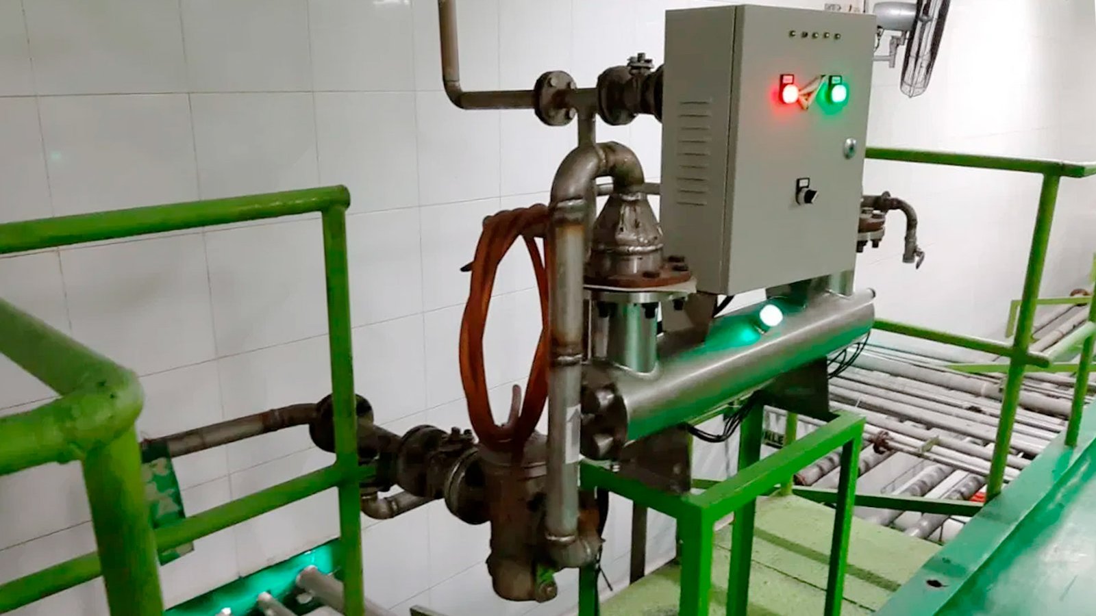 Técnico inspeccionando una planta de tratamiento de aguas residuales modular de color verde marca BIOMAX SYNERTECH, que incluye módulos de pretratamiento, decantación, DAF y oxidación avanzada. La planta está ubicada en un entorno industrial con techo alto y tuberías visibles. - ver más información